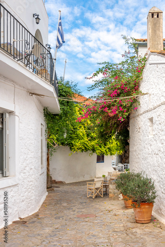 Fototapeta Naklejka Na Ścianę i Meble -  A picturesque street of stone and whitewashed homes, pink flowers, and a sidewalk cafe in the picturesque village of the small Greek island of Hydra, Greece.