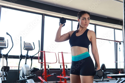 Beautiful woman exercises her arms lifting dumbbells in the gym alone determined healthy sports