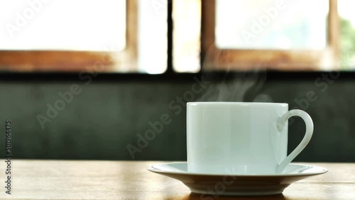 White coffee cup, hot coffee, smoke rising from the coffee cup on a wooden table on cement wall background.