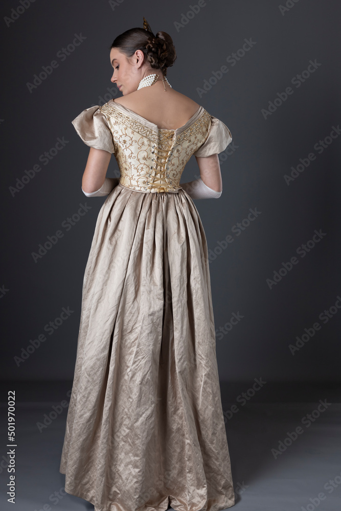 Fototapeta premium A Victorian woman wearing a gold evening gown with long, lace, fingerless gloves and standing against a studio backdrop