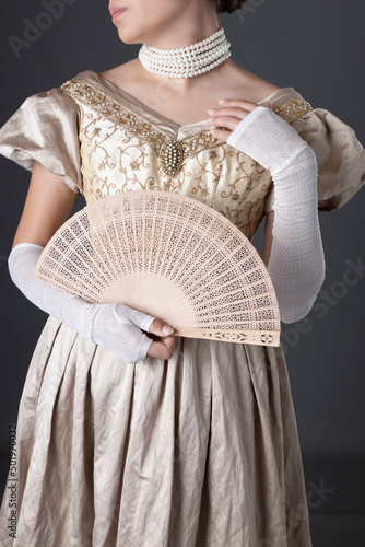A Victorian woman wearing a gold evening gown with long, lace, fingerless gloves and standing against a studio backdrop