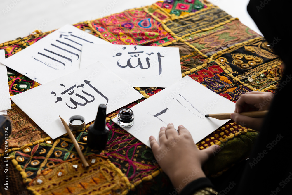 close up muslim girl hands writing Arabic text with bamboo pens and black ink on paper, Arabic letters mean the name of Muslim god close up muslim girl hands writing Arabic text with bamboo pens and black ink on paper, Arabic letters mean the name of Muslim god