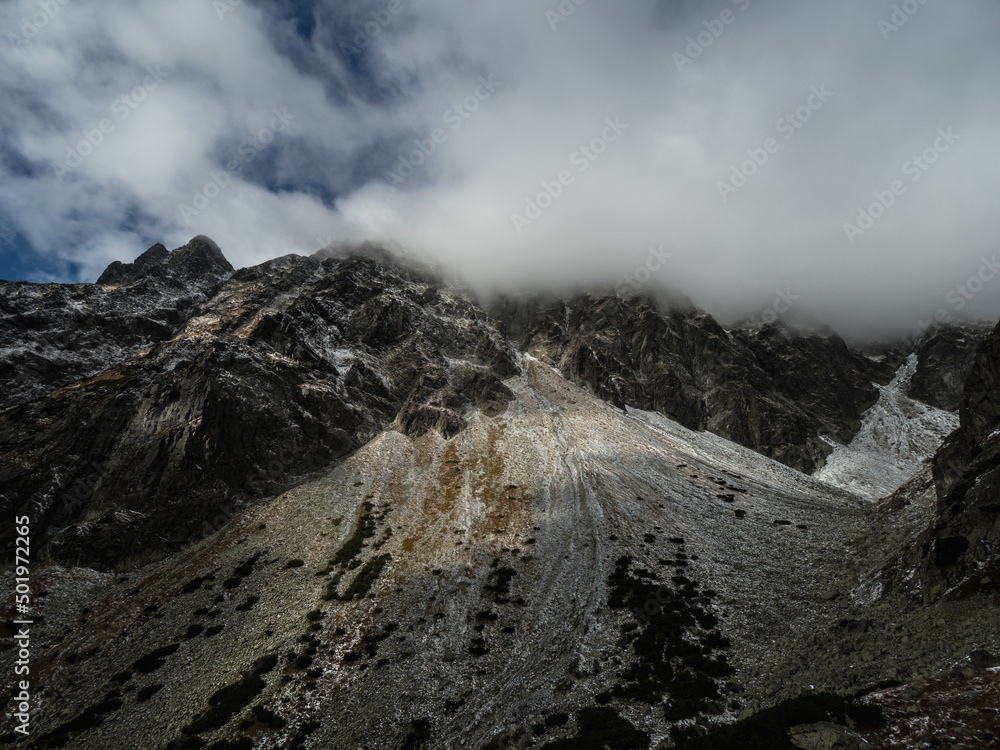 Dramatic mountains landscape with snowy mountain ridge under cloudy sky. Dark atmospheric highland scenery with high mountain range in overcast weather. Awesome mountain landscape under gray clouds.
