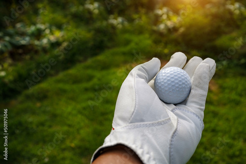 Hand-wearing golf glove holding a white golf ball on green background Large copy-space for title and text.