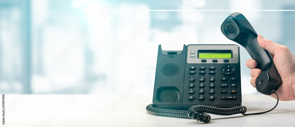 Dialing telephone keypad concept for communication, contact us and customer service support. black office voip phone with handset up on table on blurred office background. banner - obrazy, fototapety, plakaty 