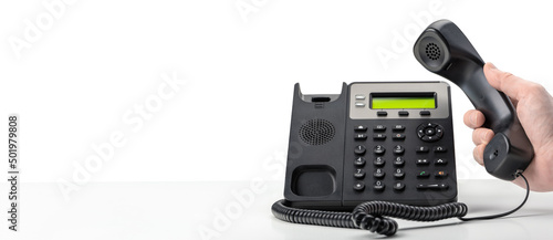 Dialing telephone keypad concept for communication, contact us and customer service support. hand holding landline voip telephone receiver on white background. banner photo