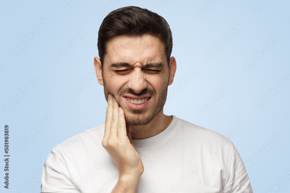 Attractive young man touches his face and closes eyes with expression of horrible pain