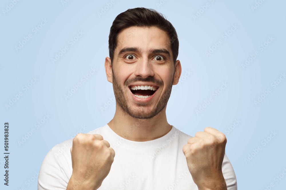 Young man shouts while his team wins raising both fists in victory gesture Young man shouts while his team wins raising both fists in victory gesture