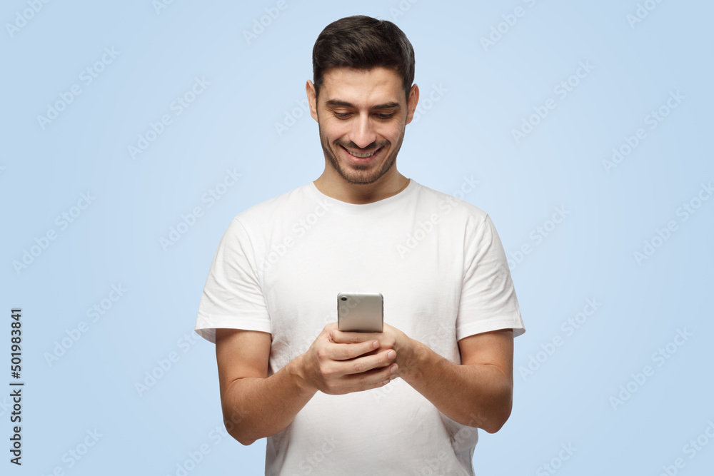 Attractive young European man looks attentively with smile at smartphone he holds Attractive young European man looks attentively with smile at smartphone he holds