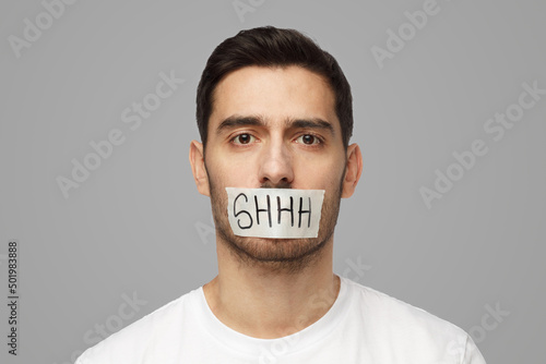 Young man with taped mouth with shhh text on it photo