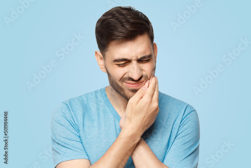 Young man feeling pain, holding his cheek with hand, suffering with painful expression