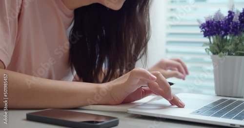 An woman Asian university college student uses a laptop computer on the table at his home.Female hands using a laptop and take notes on notepad.for studying online.Online education concept.