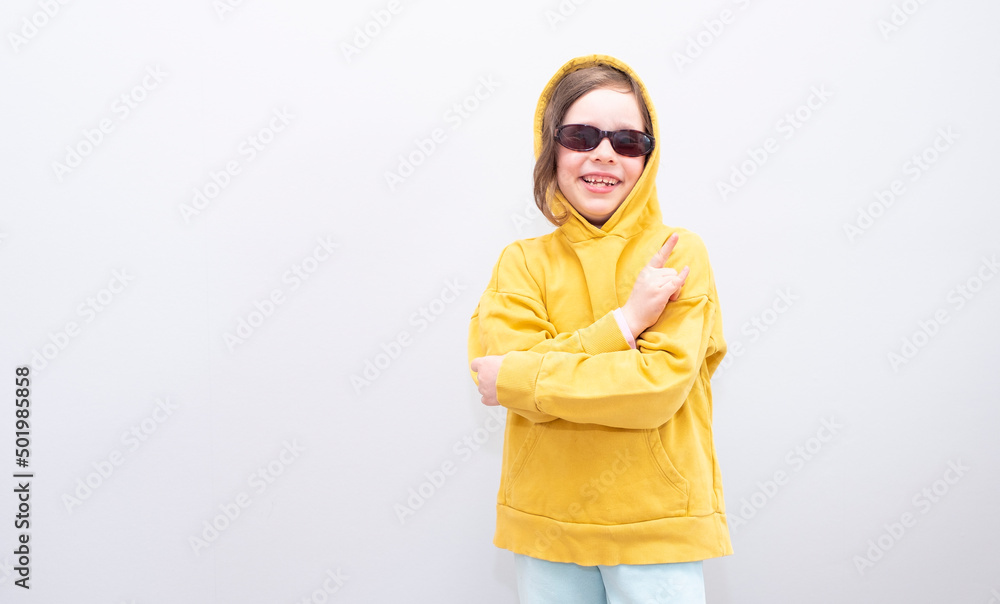 Child, Caucasian 6 years old, in a yellow sweatshirt with a hood and sunglasses on a gray background. Emotions on her face and crossed her arms on the gruli and hand gesture Child, Caucasian 6 years old, in a yellow sweatshirt with a hood and sunglasses on a gray background. Emotions on her face and crossed her arms on the gruli and hand gesture