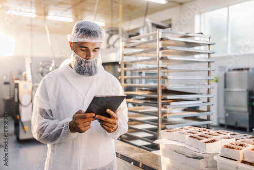 A food factory worker using tablet and checking on cookies.