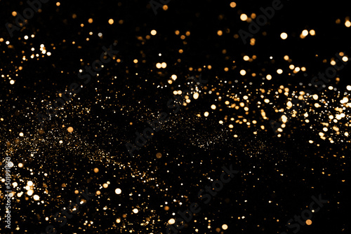 Black festive background. Abstract scattering of gold sparkles on black. Holiday backdrop, selective focus