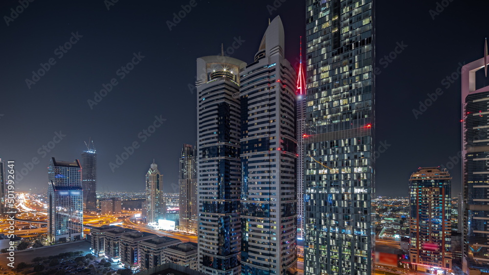 Panorama showing aerial view of Dubai International Financial District with many skyscrapers night timelapse.
