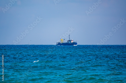 Fishing boat in blue sea and clear sky with birds flying overhead.