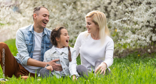 Happy family outdoors spending time together. Father, mother and daughter are having fun on a green floral grass.