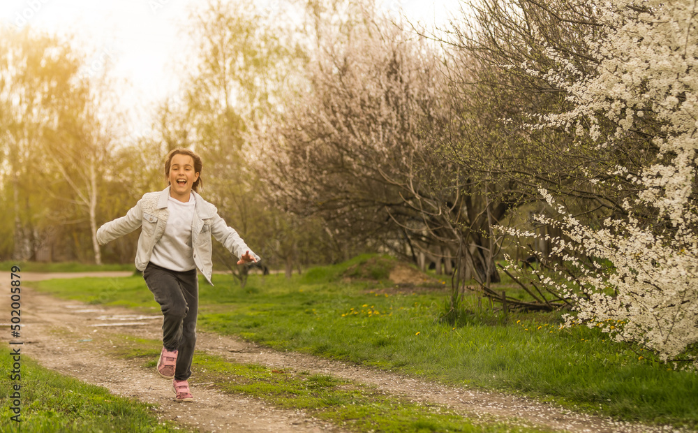 Happy little girl playing in spring cherry garden.