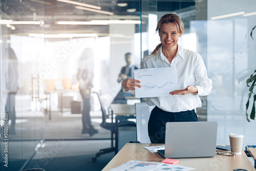 Positive mature businesswoman showing her new plans with graph in modern office 