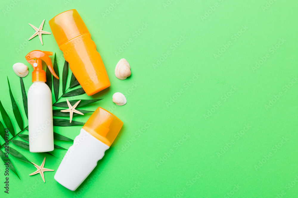 Sunscreen spray bottle. Bottle with sun protection cream and sea shells with tropical green leaf on color background, top view Sunscreen spray bottle. Bottle with sun protection cream and sea shells with tropical green leaf on color background, top view
