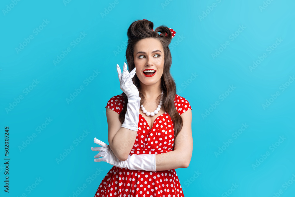 Charming pinup woman in sexy polka dot dress and gloves wearing bright makeup, posing on blue studio background Charming pinup woman in sexy polka dot dress and gloves wearing bright makeup, posing on blue studio background