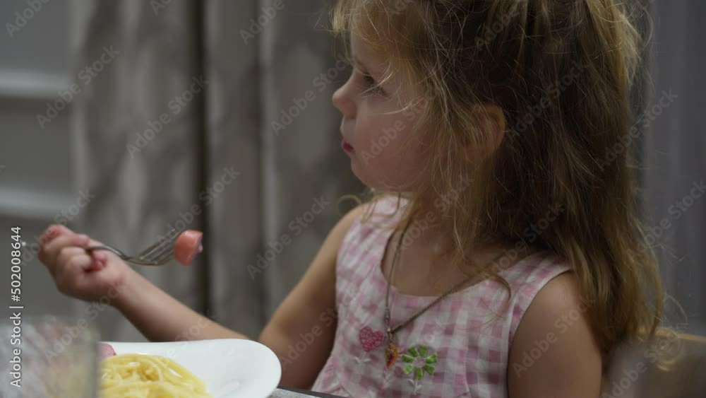 offended, capricious little girl with tears in her eyes sobs heart-rendingly and calls her mother while sitting at the dining table and eating a sausage in the living room offended, capricious little girl with tears in her eyes sobs heart-rendingly and calls her mother while sitting at the dining table and eating a sausage in the living room