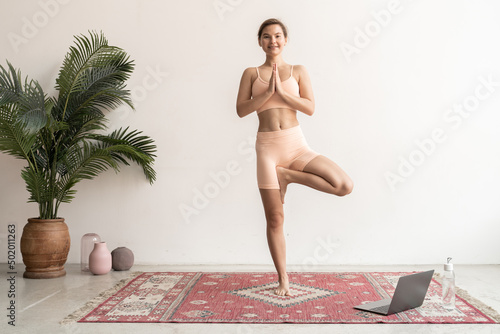 Young woman practicing yoga tree, vrikshasana pose, hands in namaste photo