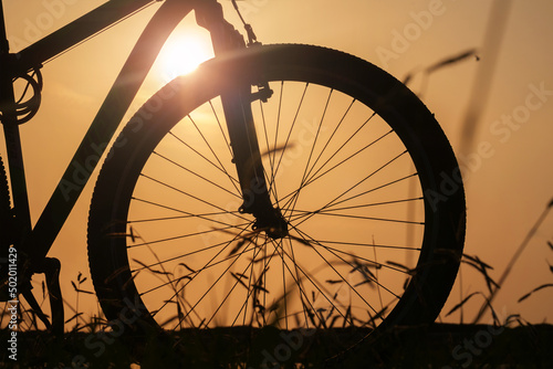 Close-up silhouette of a bike wheel at sunset. The sun shines through the frame of a bicycle, selective focus