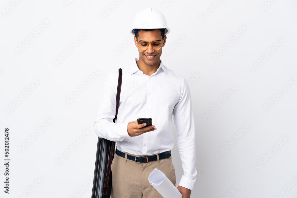 African American architect man with helmet and holding blueprints over isolated white background _ sending a message with the mobile African American architect man with helmet and holding blueprints over isolated white background _ sending a message with the mobile