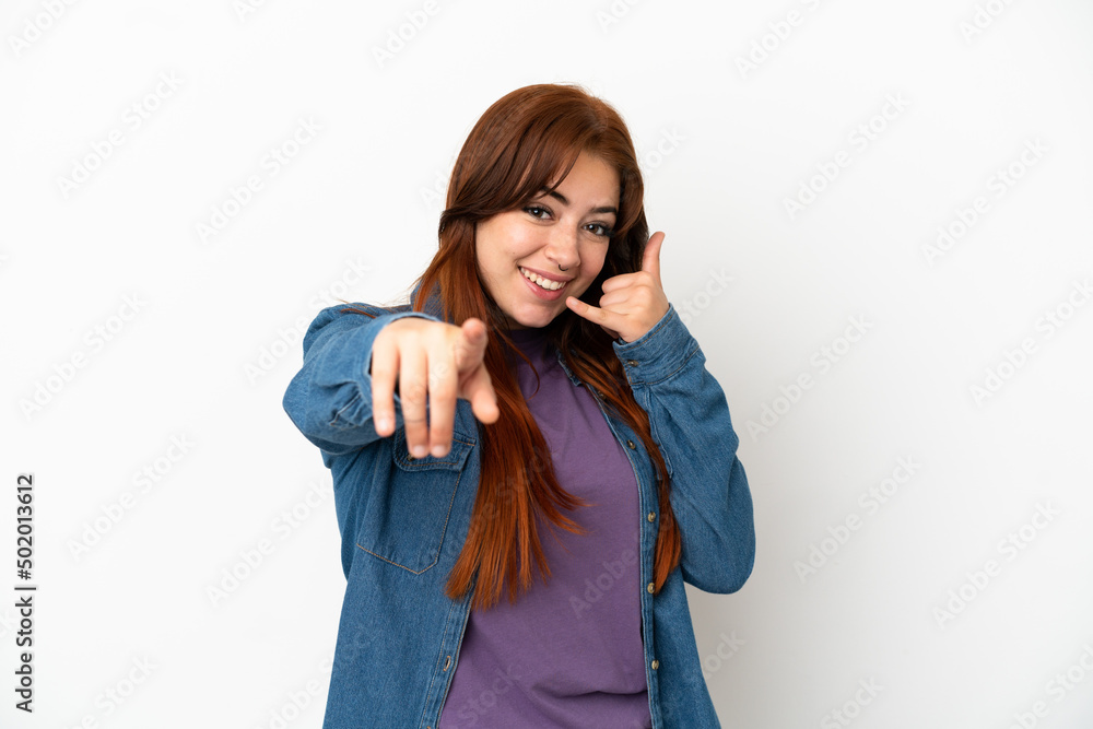 Young redhead woman isolated on white background making phone gesture and pointing front