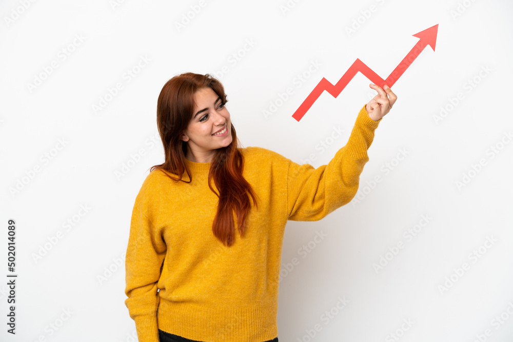 Young redhead woman isolated on white background holding a catching a rising arrow with happy expression Young redhead woman isolated on white background holding a catching a rising arrow with happy expression