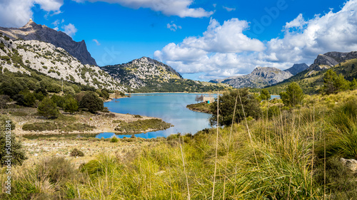 Panorama view over artificial lake Embassament de Cúber at the hiking trail GR-221 with hiking retreat Refugi de Cúber located at the grassy lake shore with mountains in the background. photo