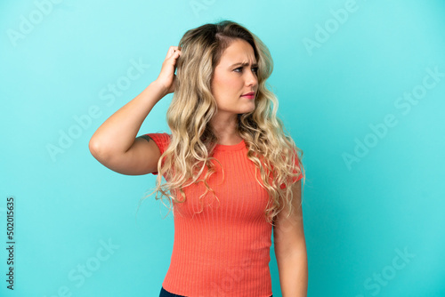 Young Brazilian woman isolated on blue background having doubts while scratching head © luismolinero