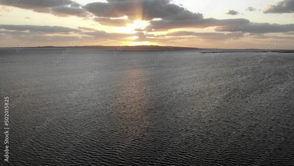 Sunset by the sea. We see a calm sea level. There are clouds in the sky behind which the setting sun is hiding. Sunset by the sea. We see a calm sea level. There are clouds in the sky behind which the setting sun is hiding.