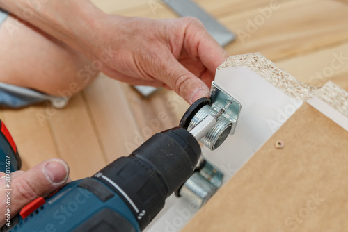 Woodwork repairman assembling a furniture using a drill.