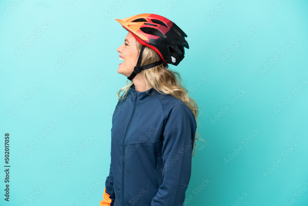 Young cyclist woman isolated on blue background laughing in lateral position Young cyclist woman isolated on blue background laughing in lateral position
