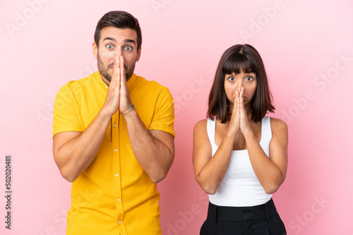 Young couple isolated on pink background keeps palm together. Person asks for something