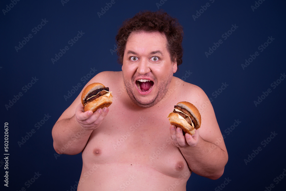 Sport, fitness and healthy lifestyle. Funny fat guy goes in for sports and eats a hamburger. Sport, fitness and healthy lifestyle. Funny fat guy goes in for sports and eats a hamburger.