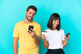 Young couple isolated on blue background buying with the mobile with a credit card