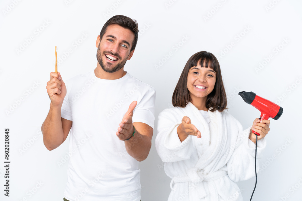Young caucasian couple holding a hairdryer and toothbrush isolated on white background shaking hands for closing a good deal Young caucasian couple holding a hairdryer and toothbrush isolated on white background shaking hands for closing a good deal