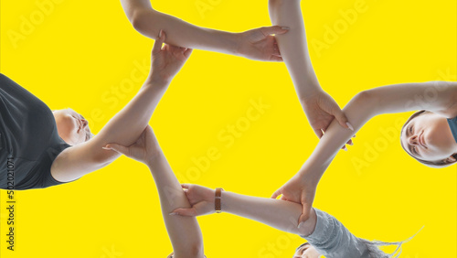 Friends join their wrist and make a circle on a yellow background. Strong friendship concept.