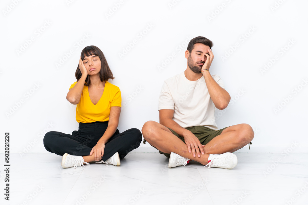 Young couple sitting on the floor isolated on white background with surprise and shocked facial expression