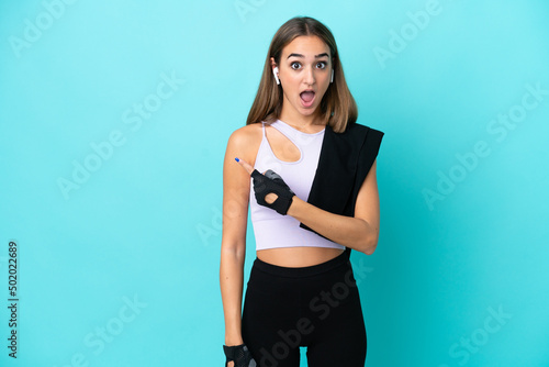 Young sport woman isolated on blue background surprised and pointing side © luismolinero