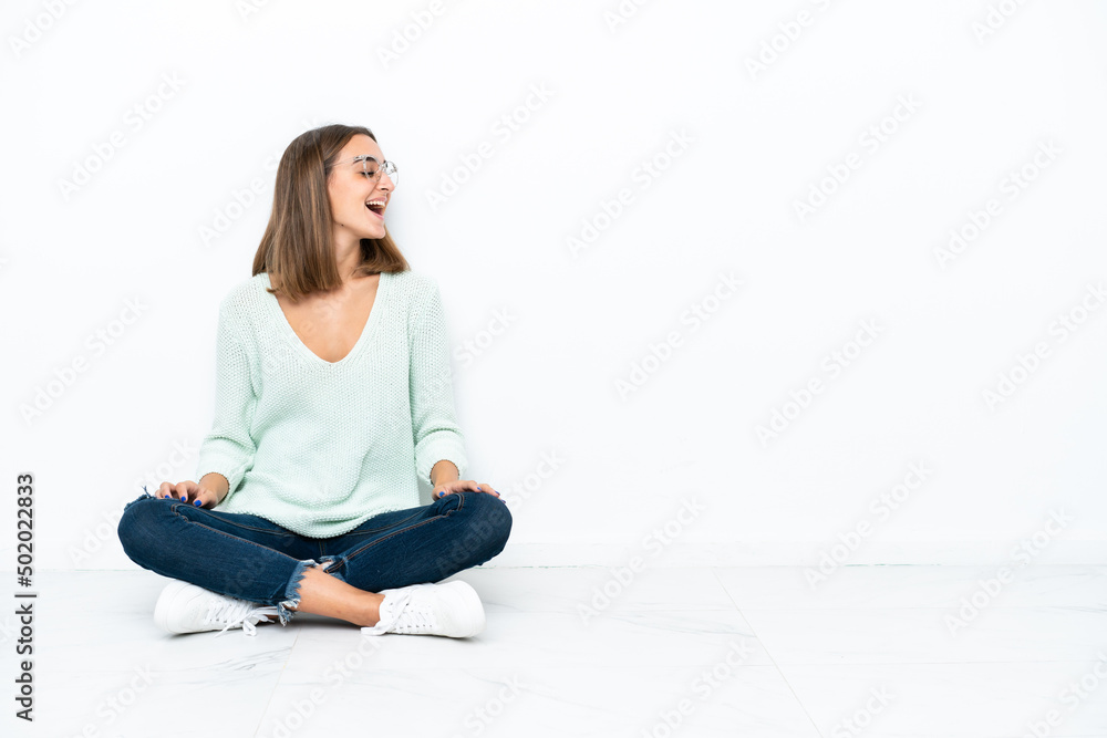 Young caucasian woman sitting on the floor isolated on white background laughing in lateral position Young caucasian woman sitting on the floor isolated on white background laughing in lateral position