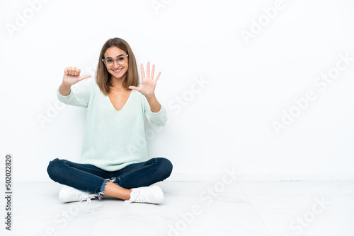 Young caucasian woman sitting on the floor isolated on white background counting six with fingers