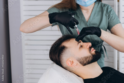 Mesotherapy procedure. A cosmetologist performs a mesotherapy procedure on the head of a young man. Hair strengthening and growth.