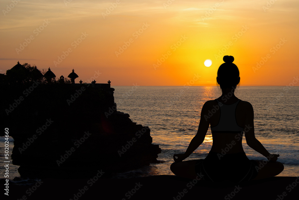 Woman silhouette in Yoga Meditating pose at orange sunset with temple shadows