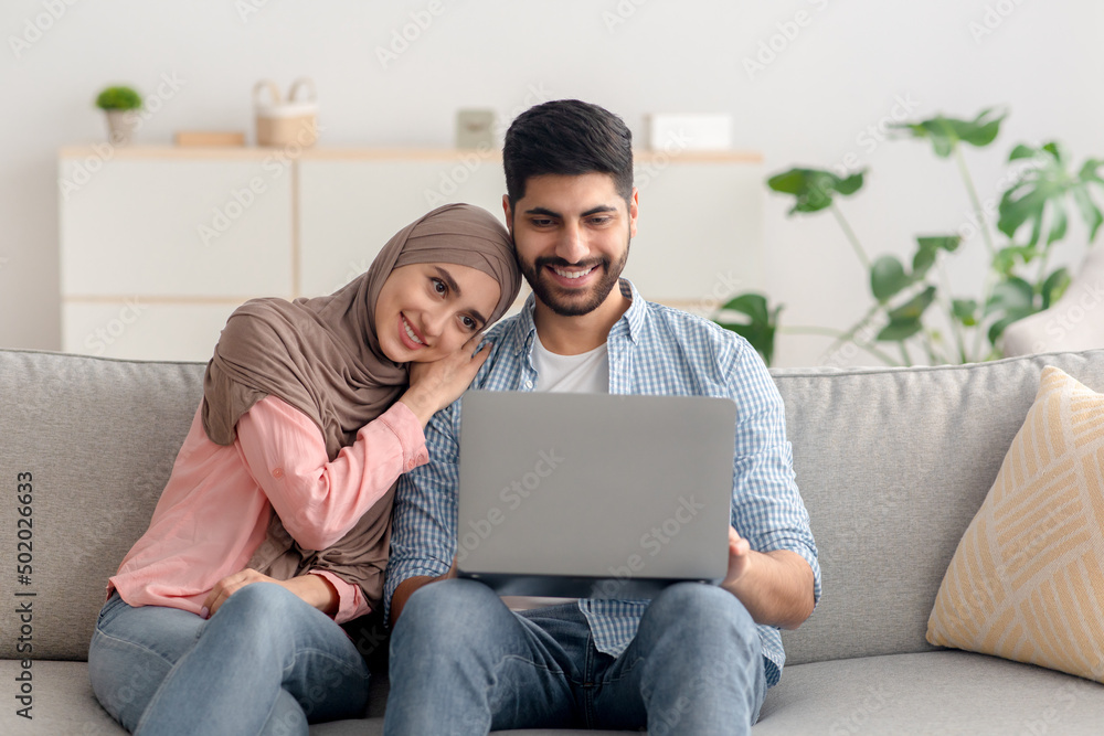 Happy Middle Eastern Spouses Using Laptop Sitting At Home Happy Middle Eastern Spouses Using Laptop Sitting At Home