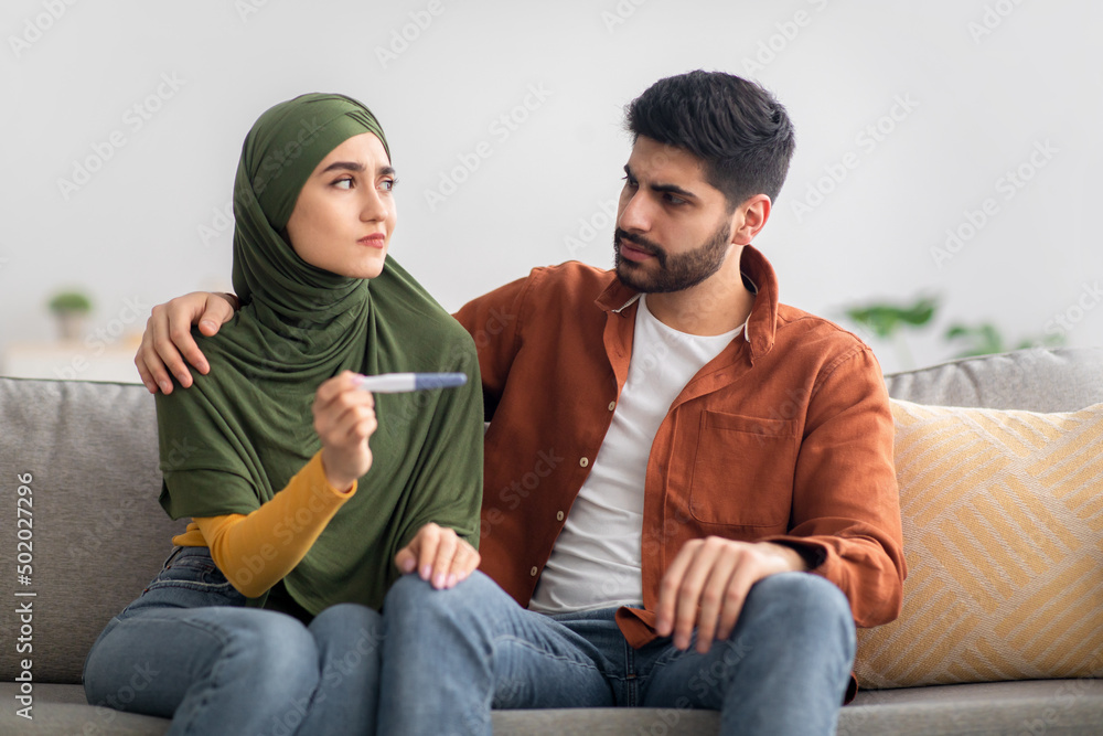 Unhappy Middle Eastern Couple Holding Negative Pregnancy Test Sitting Indoor Unhappy Middle Eastern Couple Holding Negative Pregnancy Test Sitting Indoor